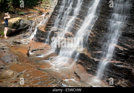 Girl taking photo of waterfall in tropical rainforest region of Borneo. Long exposure photography effect creates silky smooth waterfalls with woman Stock Photo