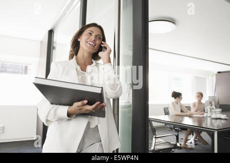 Young businesswoman with portfolio chatting on smartphone Stock Photo
