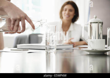 Young businesswomen pouring glass of water in conference room Stock Photo