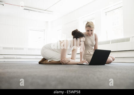 Two young businesswomen using laptop on floor in new office Stock Photo
