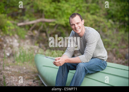 Portrait of young man sitting on upturned boat Stock Photo