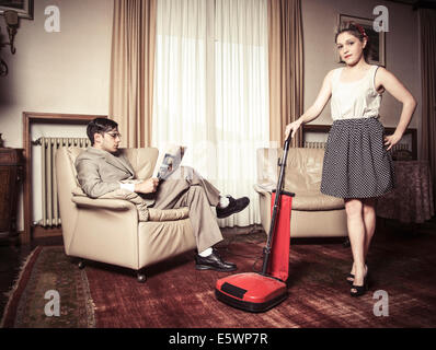 Portrait of young vintage couple in sitting room with vacuum cleaner Stock Photo