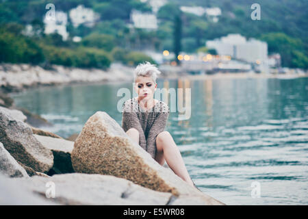 Young woman sitting alone on harbor rocks Stock Photo