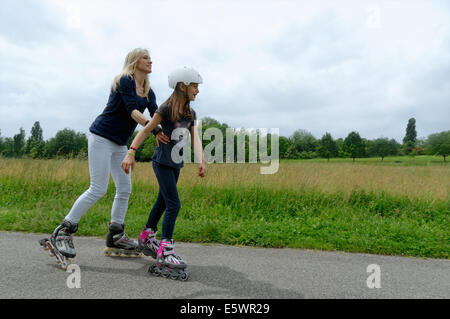 Mother holding onto daughter whilst rollerblading in park Stock Photo