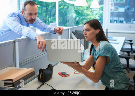 Man leaning over screen partition pointing at laptop computer Stock Photo