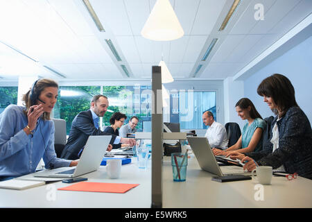Businesspeople sitting on opposite sides of screen partition, working Stock Photo