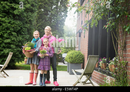 Mother and daughters outside house holding plants Stock Photo