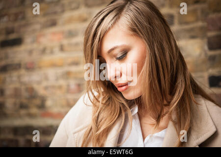 Woman with downcast eyes, brick wall in background Stock Photo