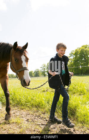 Smiling boy leading horse along dirt track Stock Photo