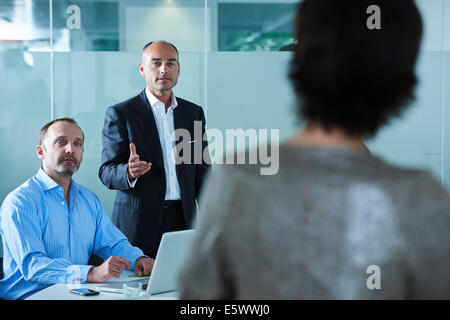 Businessmen and women debating across boardroom table Stock Photo