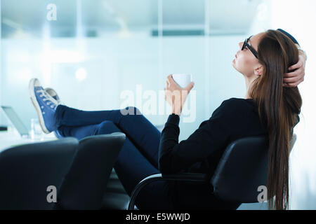 Female office worker leaning back with feet up on conference table Stock Photo