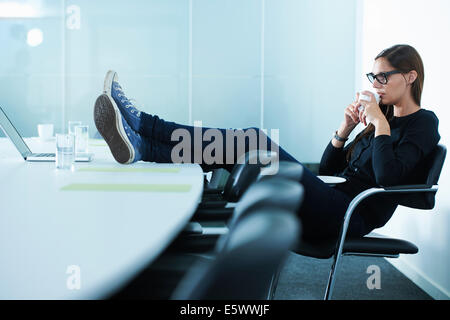 Female office worker drinking coffee with feet up on conference table Stock Photo
