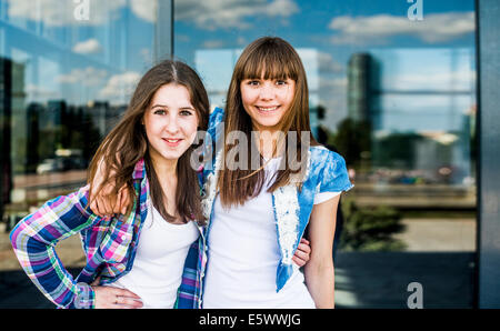Portrait of two smiling young women in front of glass fronted office building Stock Photo