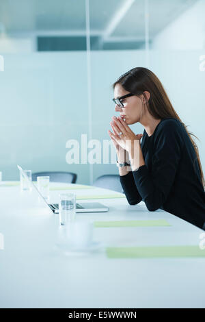 Worried female office worker using laptop at conference table Stock Photo