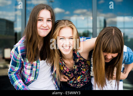 Portrait of three young women laughing in front of glass office building Stock Photo