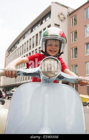 Portrait of ten year old boy pretending to ride motor scooter on city street Stock Photo