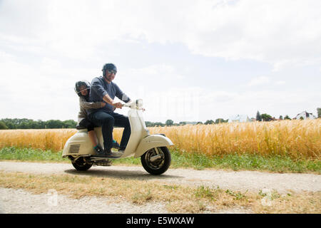 Mature man and daughter riding motor scooter along dirt track Stock Photo