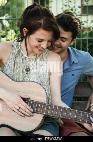Young couple serenading on acoustic guitar in park Stock Photo