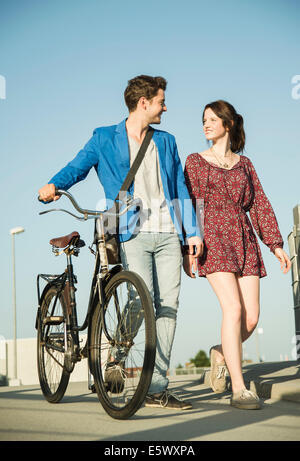 Young couple pushing bicycle along street Stock Photo