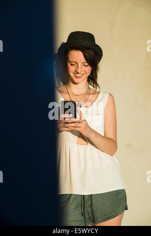 Young woman leaning against wall reading text on smartphone Stock Photo