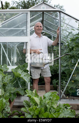 Portrait of senior man in his garden greenhouse with watering can Stock Photo