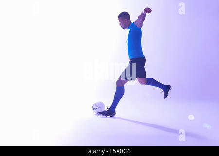 Studio shot of young male soccer player with arms outstretched kicking the ball