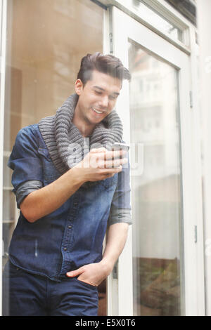 Young man texting on smartphone behind patio glass Stock Photo