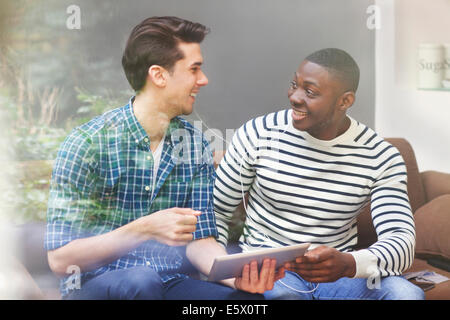 Two young male friends listening to music on digital tablet behind window Stock Photo