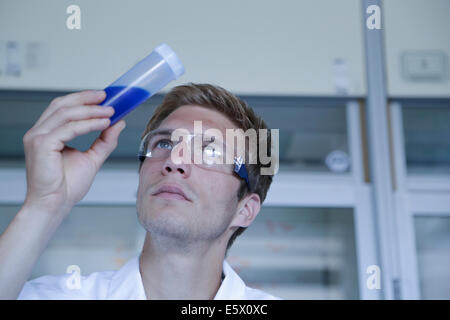 Male scientist looking up at sample in plastic bottle in lab Stock Photo