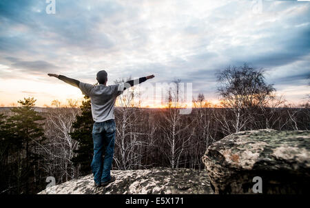 Young man with arms outstretched on top of rock formation at sunset Stock Photo