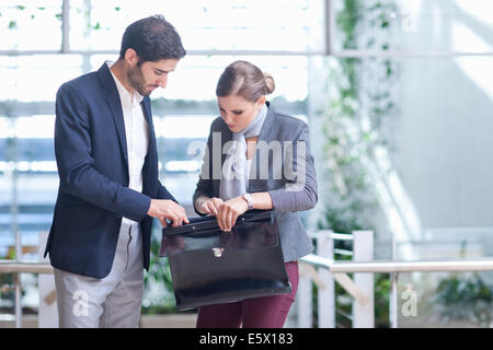 Businessman and businesswoman opening briefcase in conference centre atrium Stock Photo