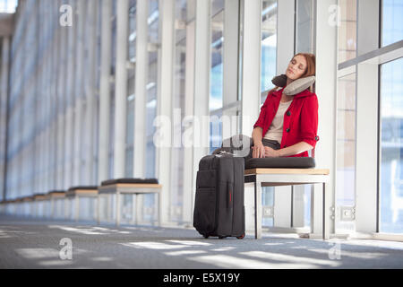 Mid adult businesswoman with wheeled case asleep in conference centre corridor Stock Photo