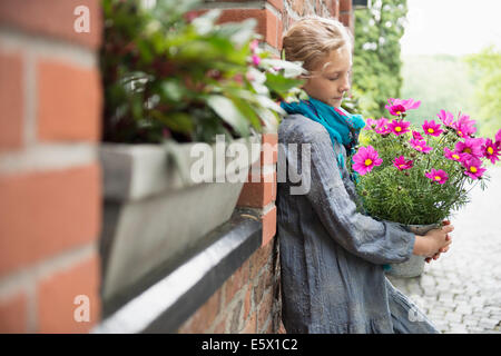 Portrait of girl leaning against wall with flower pot plant in garden Stock Photo
