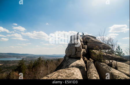 Three male hikers on top of rock formation with lake in distance Stock Photo
