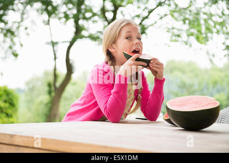 Girl at patio table eating watermelon slice Stock Photo