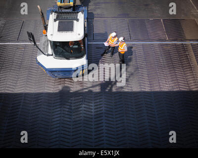 Workers in discussion with truck driver on ship's ramp, elevated view