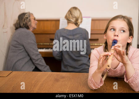 Girl playing recorder while sister on piano watched by grandmother Stock Photo