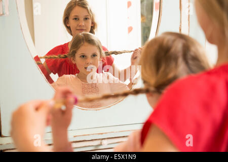 Sisters holding up plaits in bedroom mirror Stock Photo