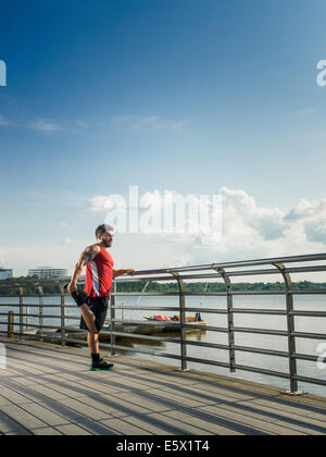 Young man doing training warm up exercises on lake pier Stock Photo