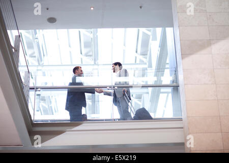 Two young businessmen shaking hands on conference centre balcony Stock Photo