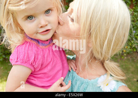Close up of young adult mother kissing toddler daughter in garden