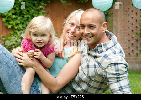 Portrait of happy couple sitting with toddler daughter in garden