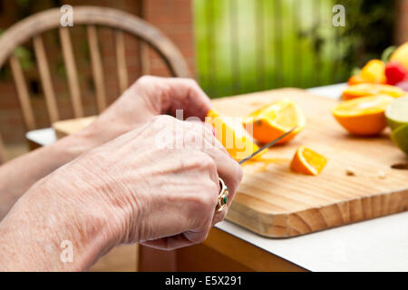 Hands of senior woman slicing oranges at garden table Stock Photo