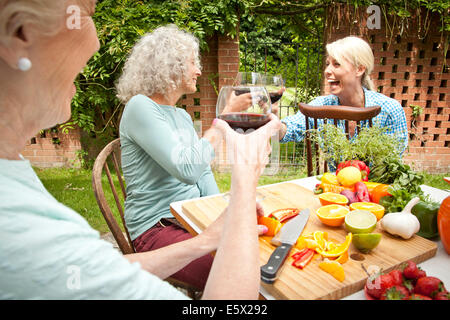 Three generation women raising a glass of red wine while preparing food at garden table Stock Photo