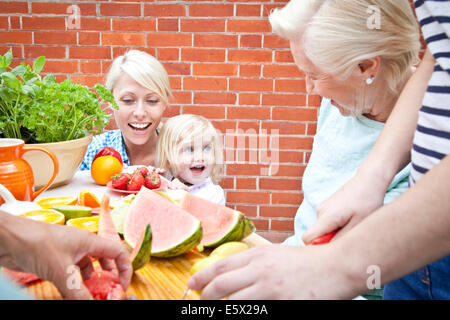 Four women and one female toddler preparing food at garden table Stock Photo