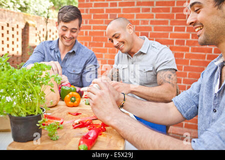 Three male friends laughing and preparing food for garden barbecue Stock Photo