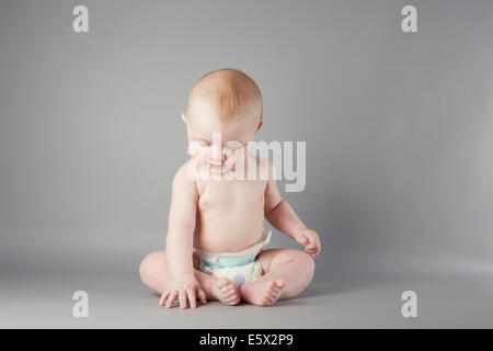 Studio portrait of baby boy sitting up and touching floor Stock Photo