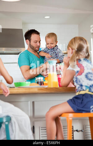 Father multi tasking breakfast with son and daughters Stock Photo
