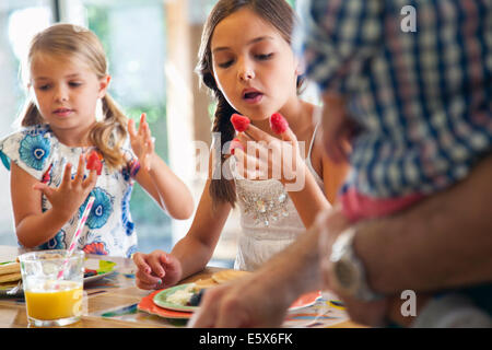 Two sisters with raspberries on their fingers at kitchen breakfast bar Stock Photo