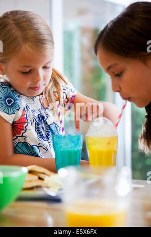 Close up of two sisters blowing bubbles through straws at breakfast bar Stock Photo